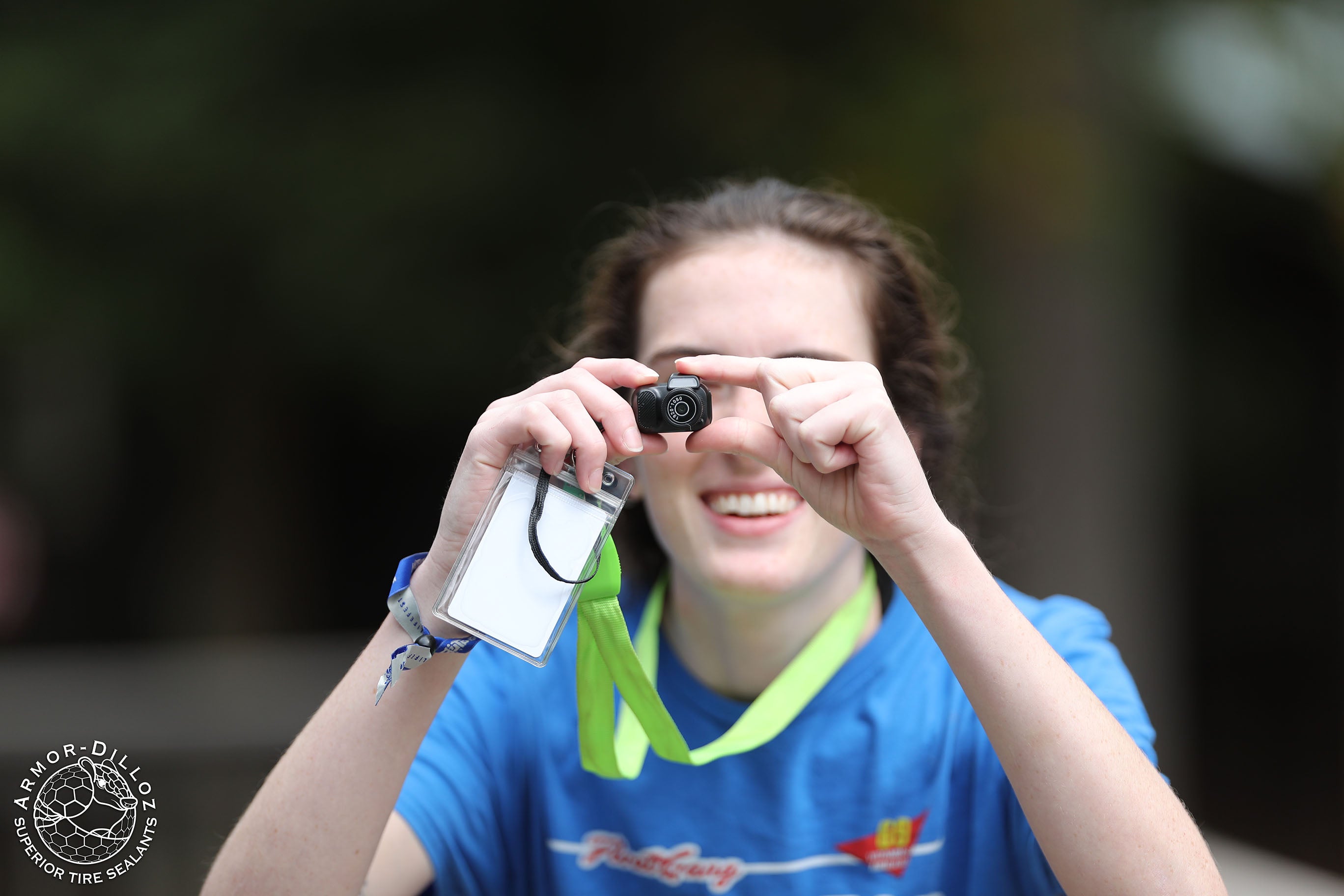 A smiling attendee in a blue shirt holds up a tiny camera at Floatlife Fest 7.