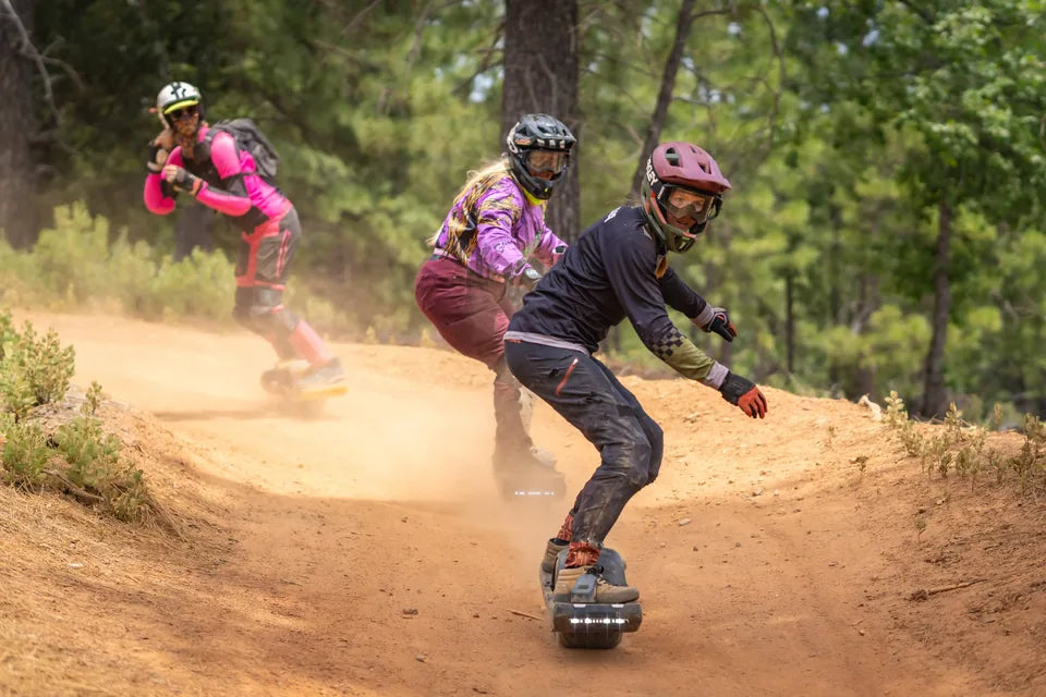 Three helmeted Onewheel racers carve a dusty forest trail during the Best of the West circuit.