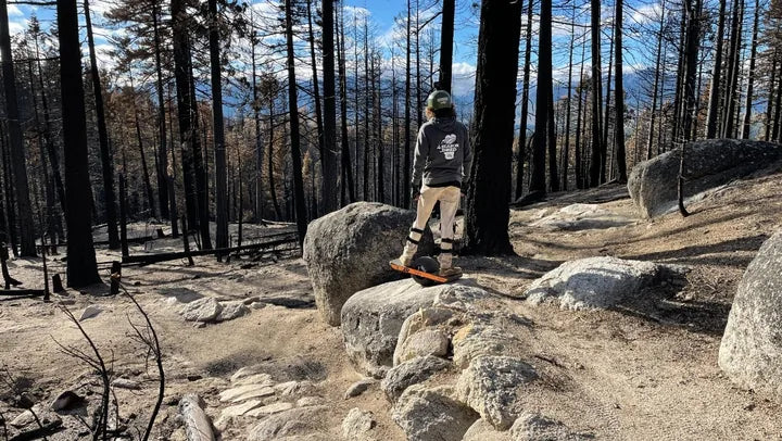 A rider stands on a Onewheel atop a boulder in the fire-scarred Corral-Sidewinder forest