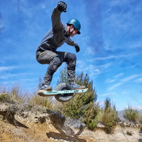 Dominique Williams jumping a Onewheel over a dirt ledge.