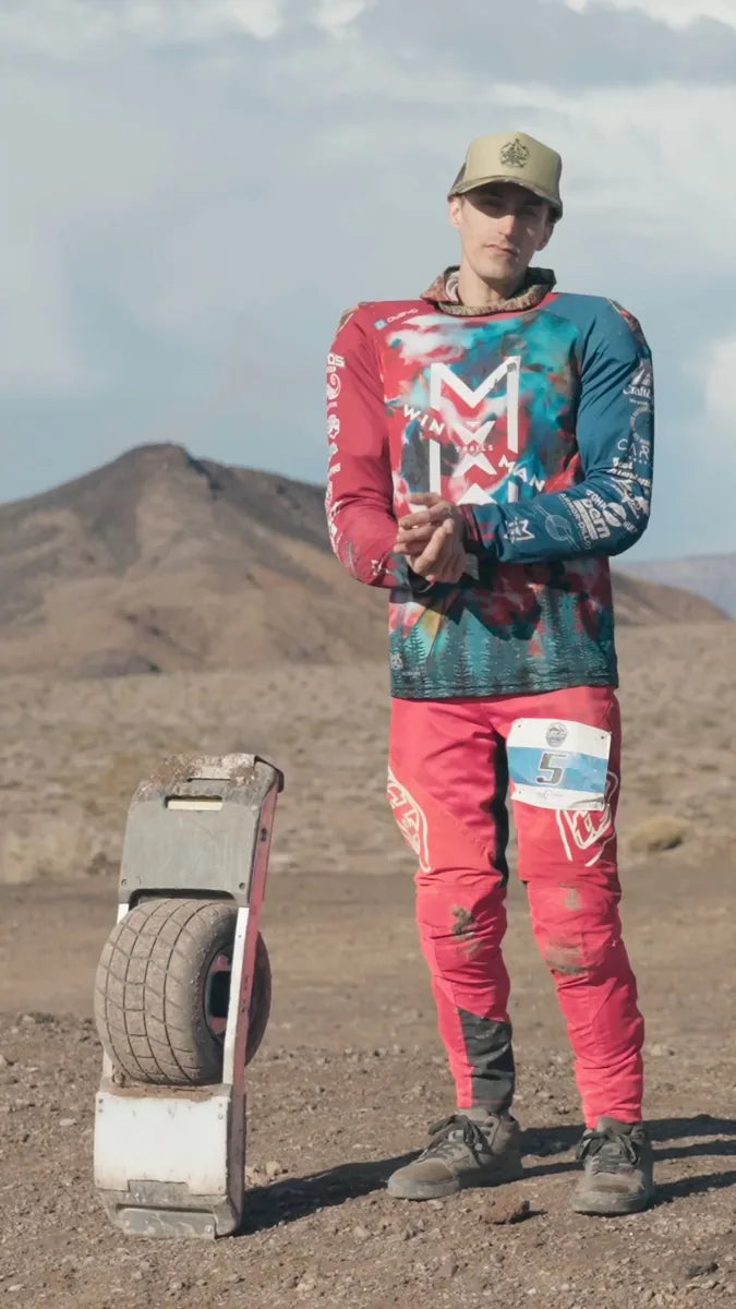 Luke Austin in race gear beside his Onewheel on a desert course.