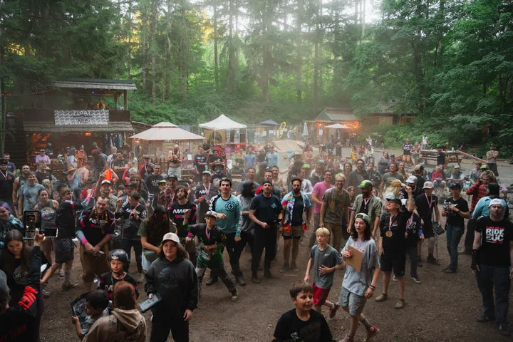 A large group of Northwest Electric Fest attendees gathers in a wooded festival area.