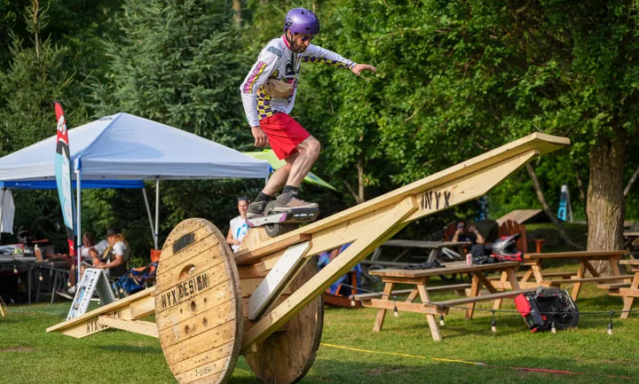 Onewheel rider balancing across a large wooden spool obstacle at the Québec Electric Games