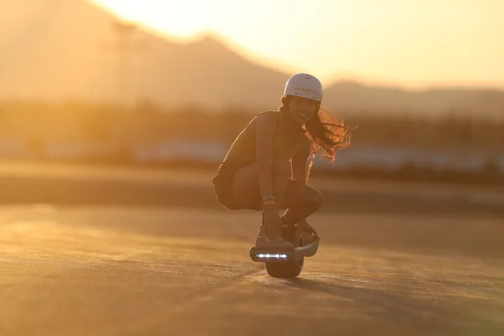 Rider walking away across a sunset field with a Onewheel