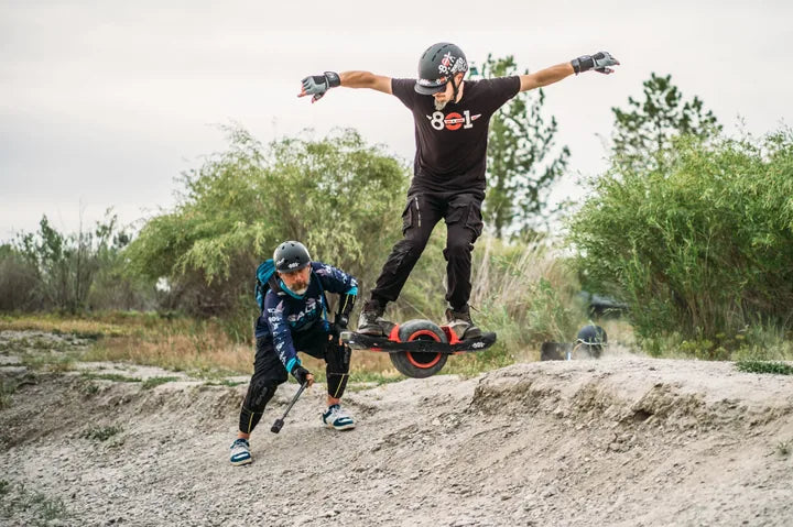 801Wheel rider launching over a dirt mound while another rider films