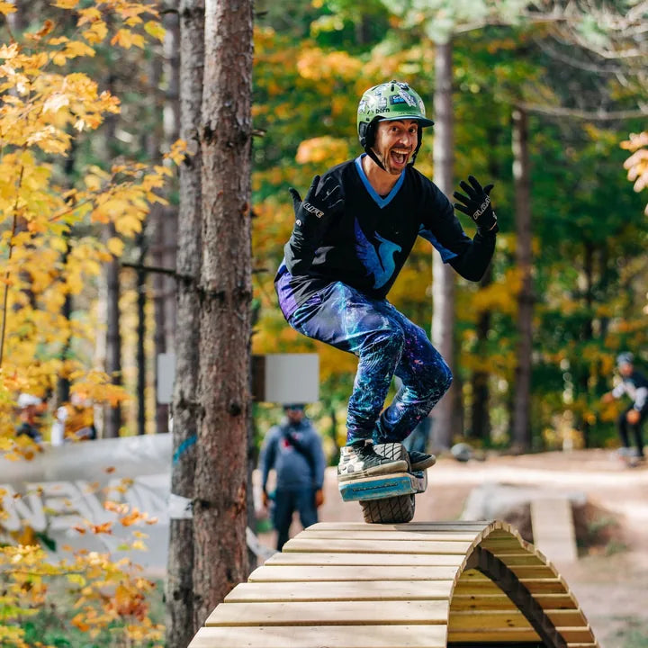 Onewheel rider crossing a wooden trail feature at WinMan