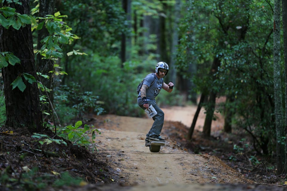 A helmeted rider speeds down a narrow dirt line between trees at Floatlife Fest 3.5.