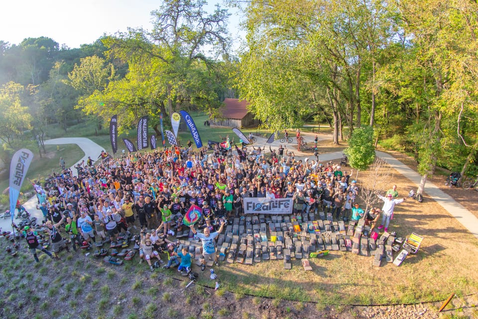 A large crowd of riders and Onewheels fills a sunny hillside for the Floatlife Fest 5 group photo.