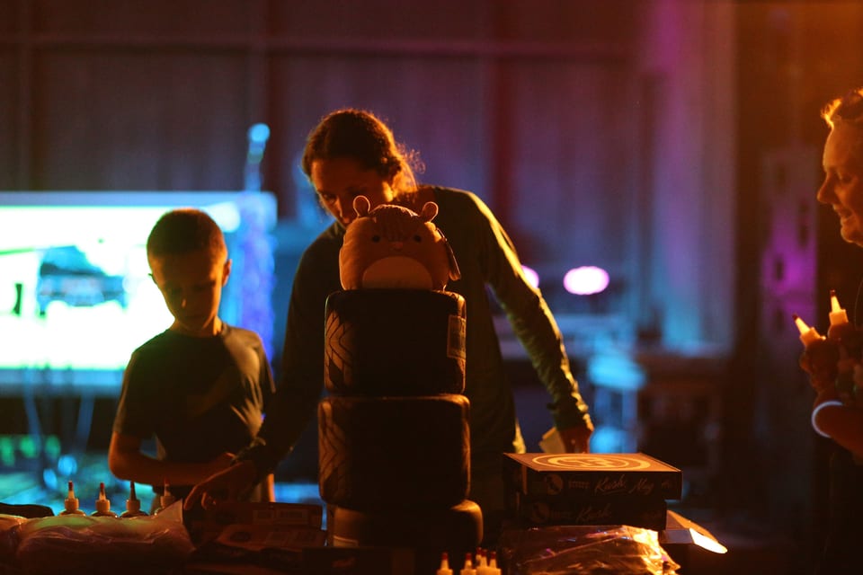People gather around an illuminated table and event booth after dark.
