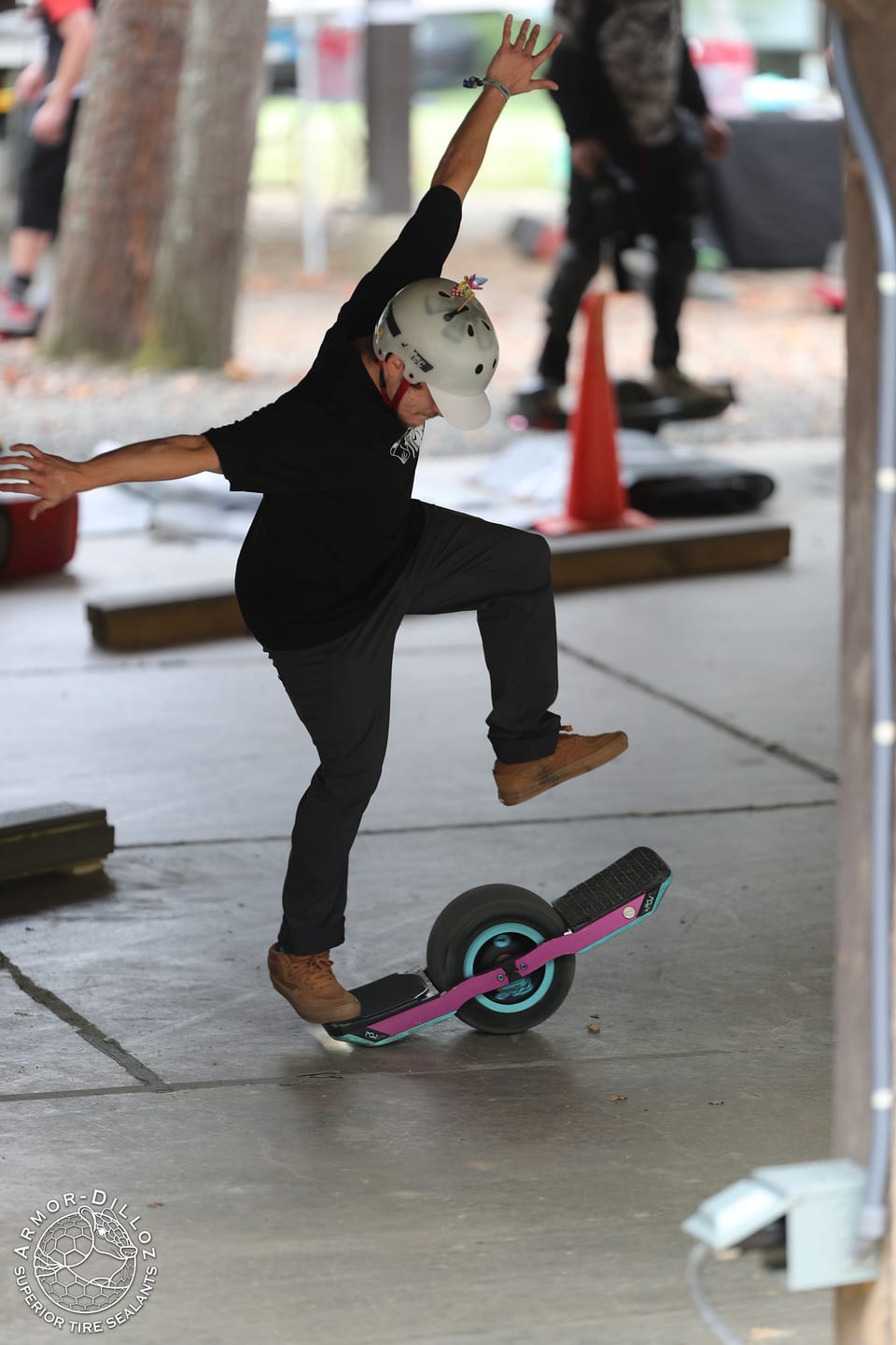 A helmeted rider balances on a purple Onewheel beneath the Floatlife Fest pavilion.