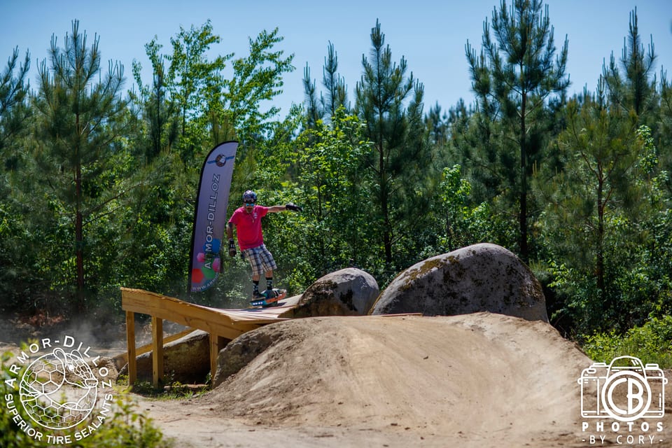 A red-shirted helmeted rider carves down a dirt roller at Oak City Shredfest.