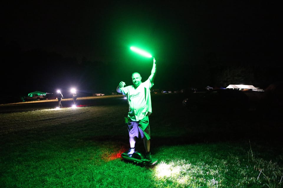 A rider holds a bright green light wand on the dark Oak City course.