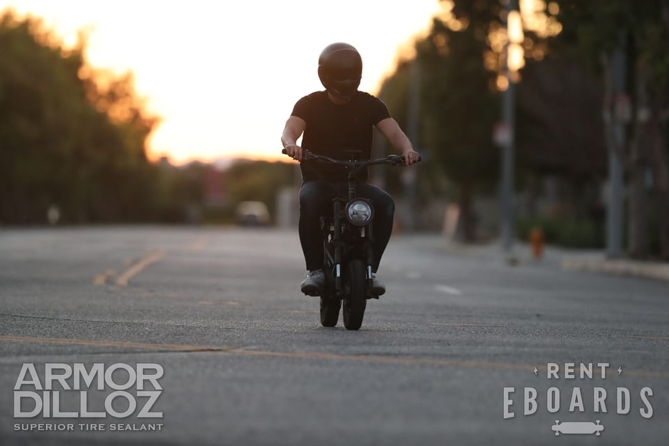 A rider lifts the front of a Onewheel against warm evening light at RiderFest.