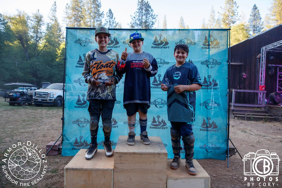 Three riders stand on the Seek N' Shred awards podium with their boards.