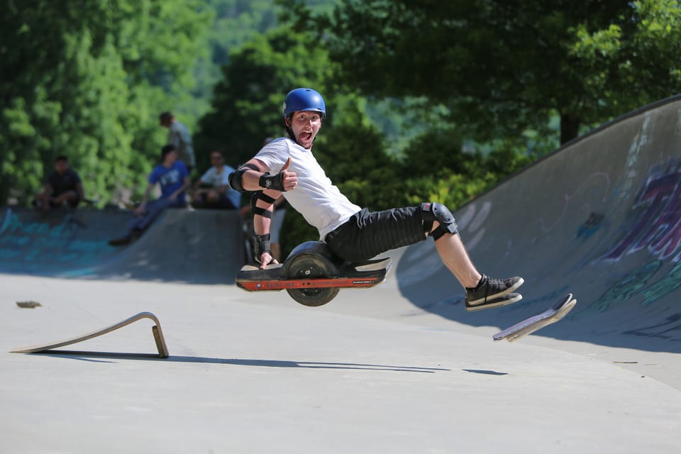 A helmeted rider leans deeply through a concrete skatepark bowl at Wheel Scorcher.