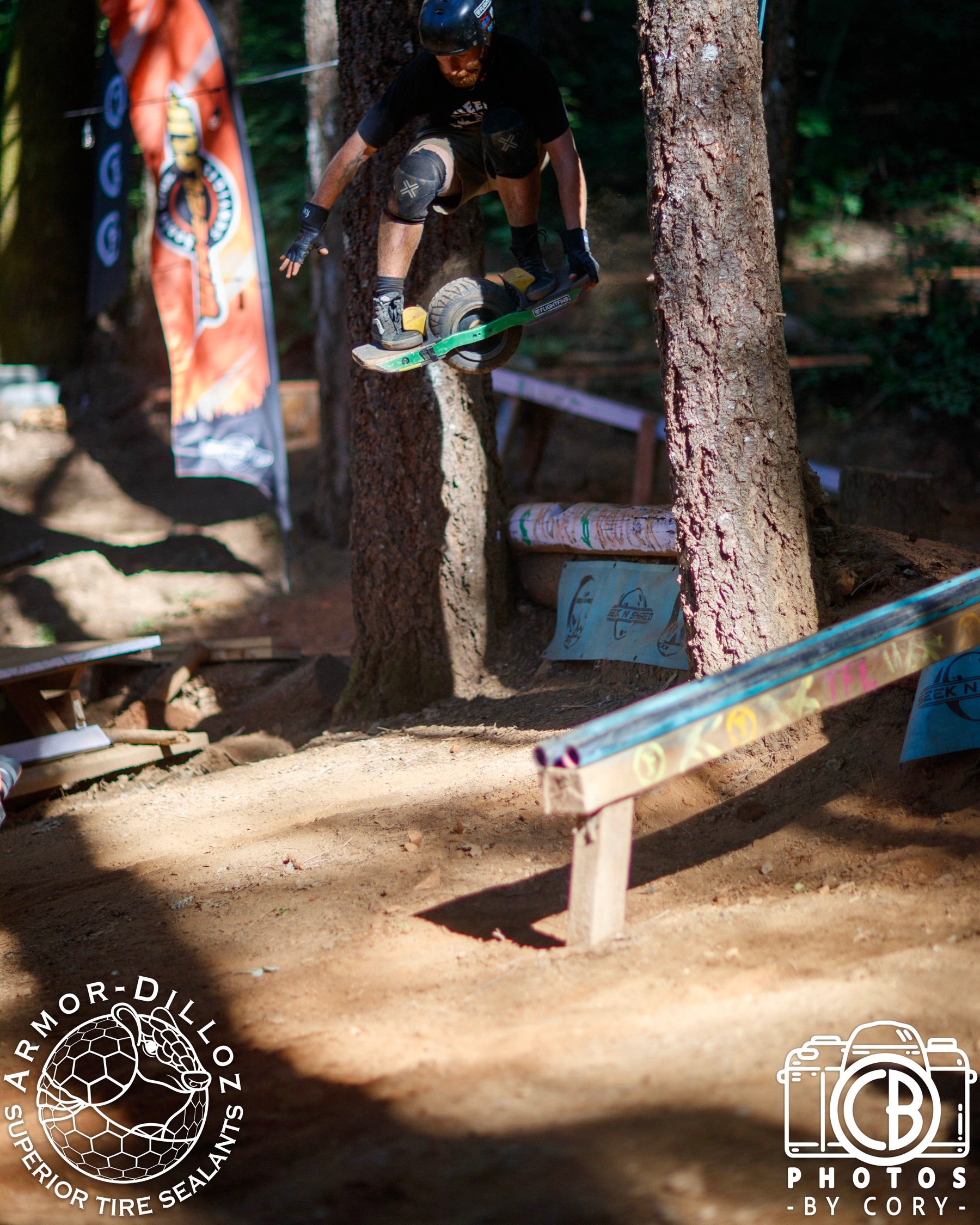 A helmeted Onewheel rider is airborne between trees on a forest race course.